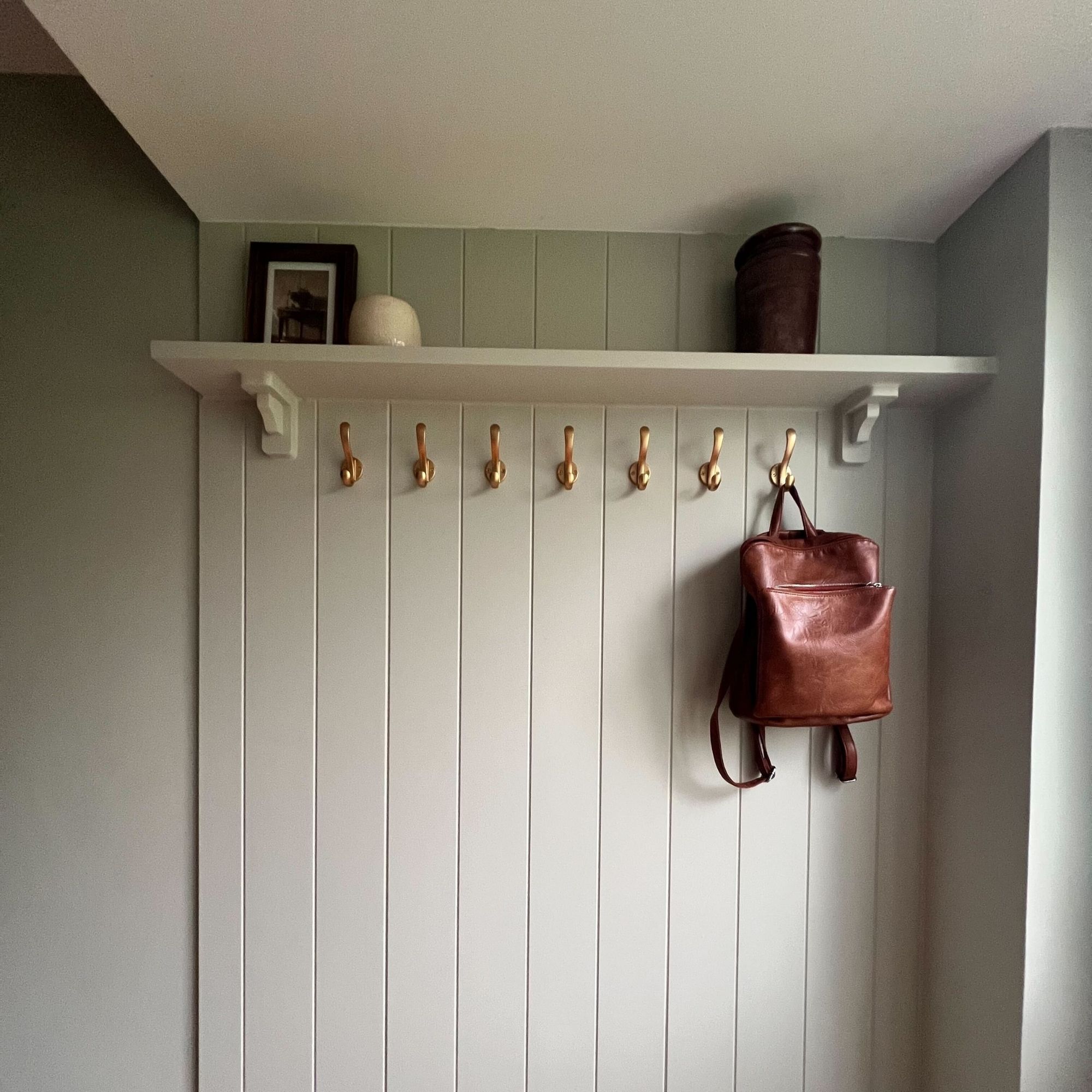 A panelled wall with gold hooks and a floating shelf.