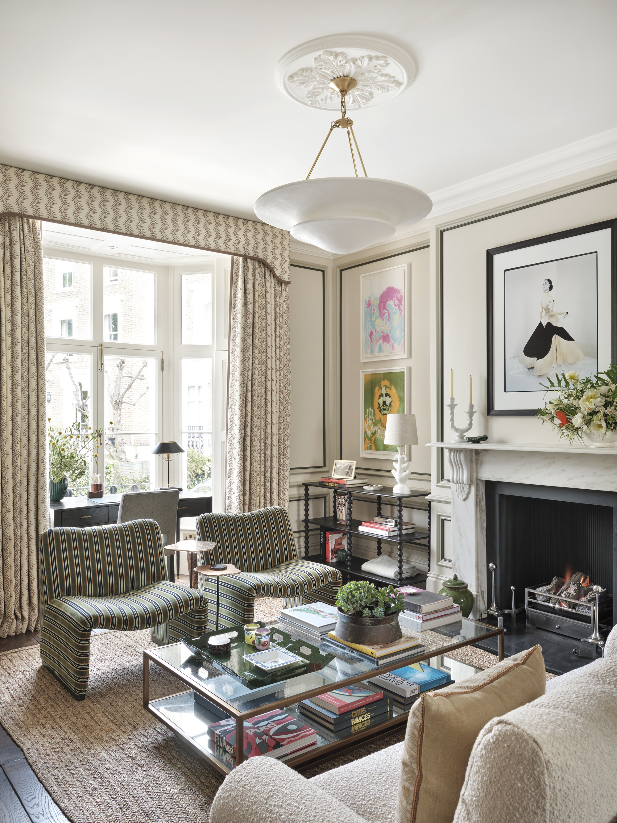 A living room with patterned curtains with a valance, a glass coffee table with books and magazines, and two patterned chairs