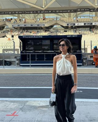 Lily Muni He at Yas Marina Circuit in Abu Dhabi wearing a white halter top, black trousers, and a Bvlgari Serpenti watch.