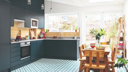 Dark green kitchen cabinets with patterned flooring and wooden dining table