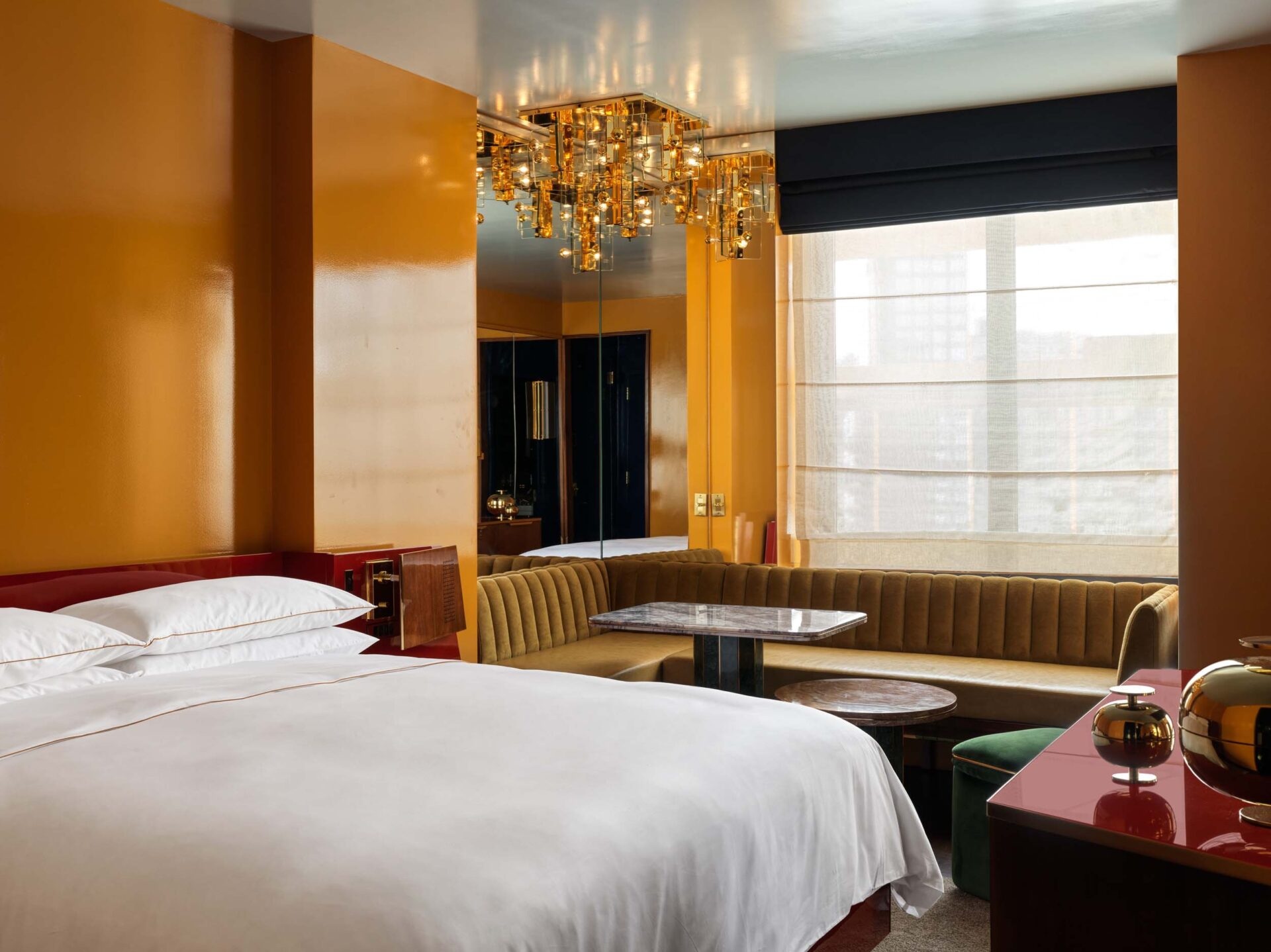 A glamorous, 1970s-inspired New York hotel boasts rooms defined by sleek, shiny surfaces, an earthy color palette, sculptural chandeliers and artwork accents, and textural details.