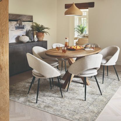 A neutral dining room with an oval dining table and a vintage-style patterned rug underneath