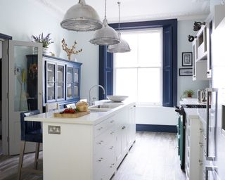 A narrow white kitchen island in front of a large blue window and metal pendant lights