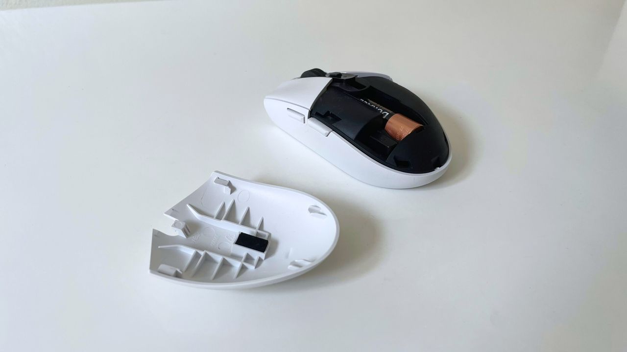 The Logitech G305 LIGHTSPEED wireless mouse with battery cover removed sitting on a white desk