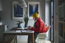  man sitting working from home in a red puffer coat, scarf and wooly hat
