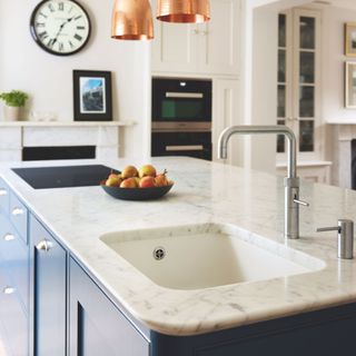 Close up of marble kitchen island with blue cabinets underneath and a bowl of pears on top