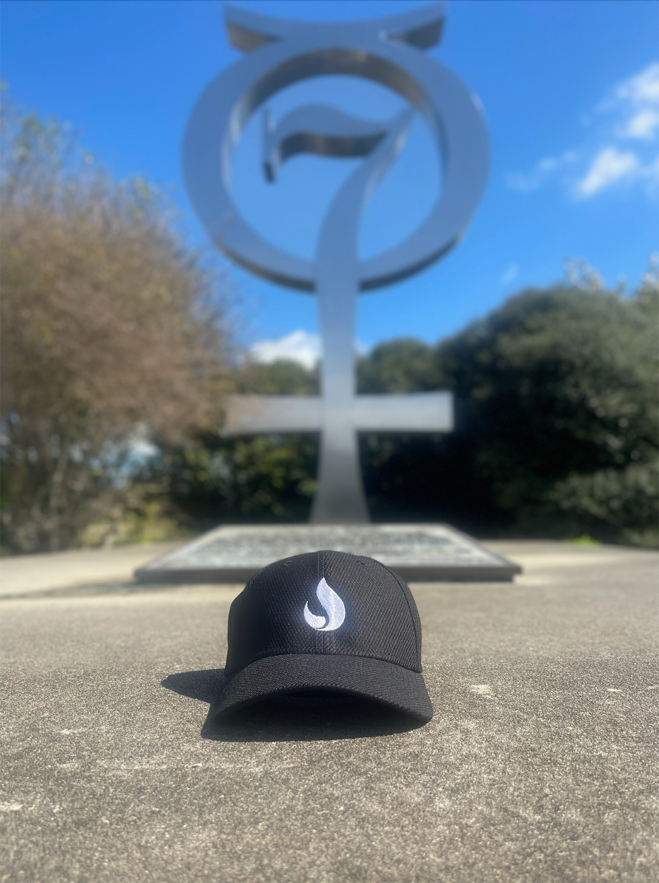 A baseball cap with the Stoke Space logo sits on the ground in front of the Project Mercury sculpture at the entrance to Launch Complex 14 (LC-14) at Cape Canaveral Space Force Station.