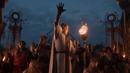 Divinity trailer screenshot showing a mysterious masked figure reaching out with an audience behind him