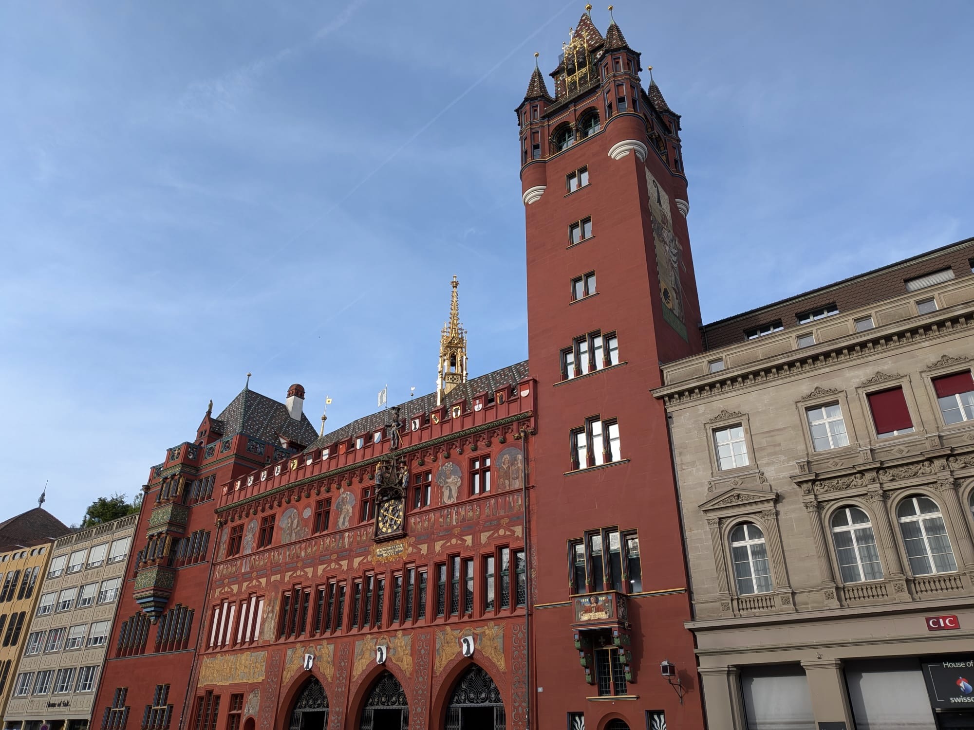 Rathaus in Basel, a red building with gold decorations and frescos and a tower, which serves as a government building.