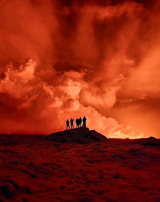 Local resident watch smoke billow as the lava colour the night sky orange from an volcanic eruption on the Reykjanes peninsula 3 km north of Grindavik, western Iceland on December 19, 2023