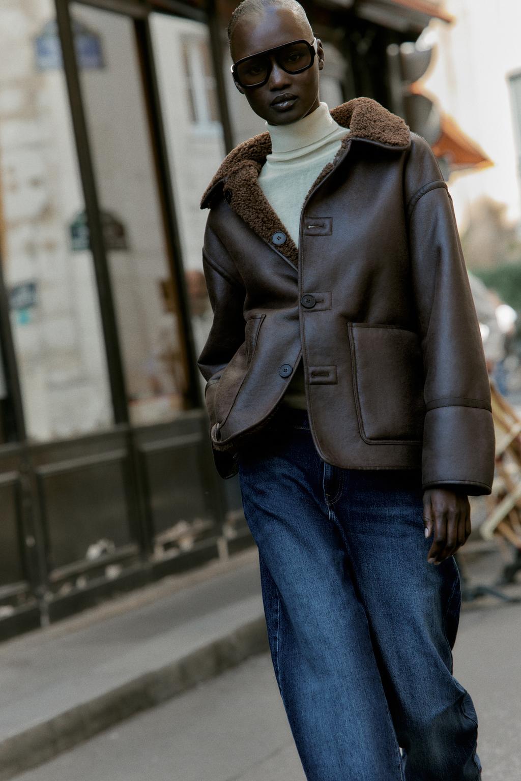 Woman wears cream turtleneck jumper, brown borg jacket and blue jeans