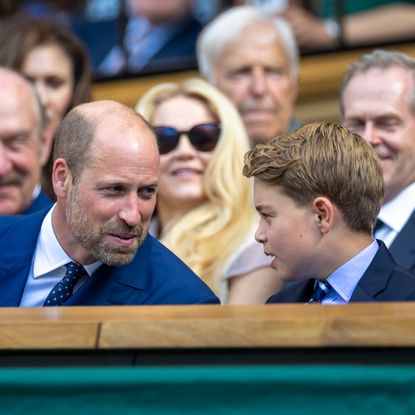Prince William smiling sitting next to Prince George at Wimbledon and leaning towards him