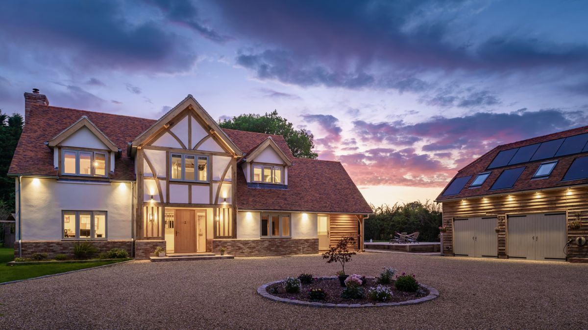 evening shot of large oak frame house with render and oak exterior, tiled roof and separate double garage building to side with large gravel driveway in front of both buildings