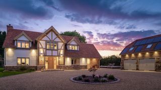 evening shot of large oak frame house with render and oak exterior, tiled roof and separate double garage building to side with large gravel driveway in front of both buildings