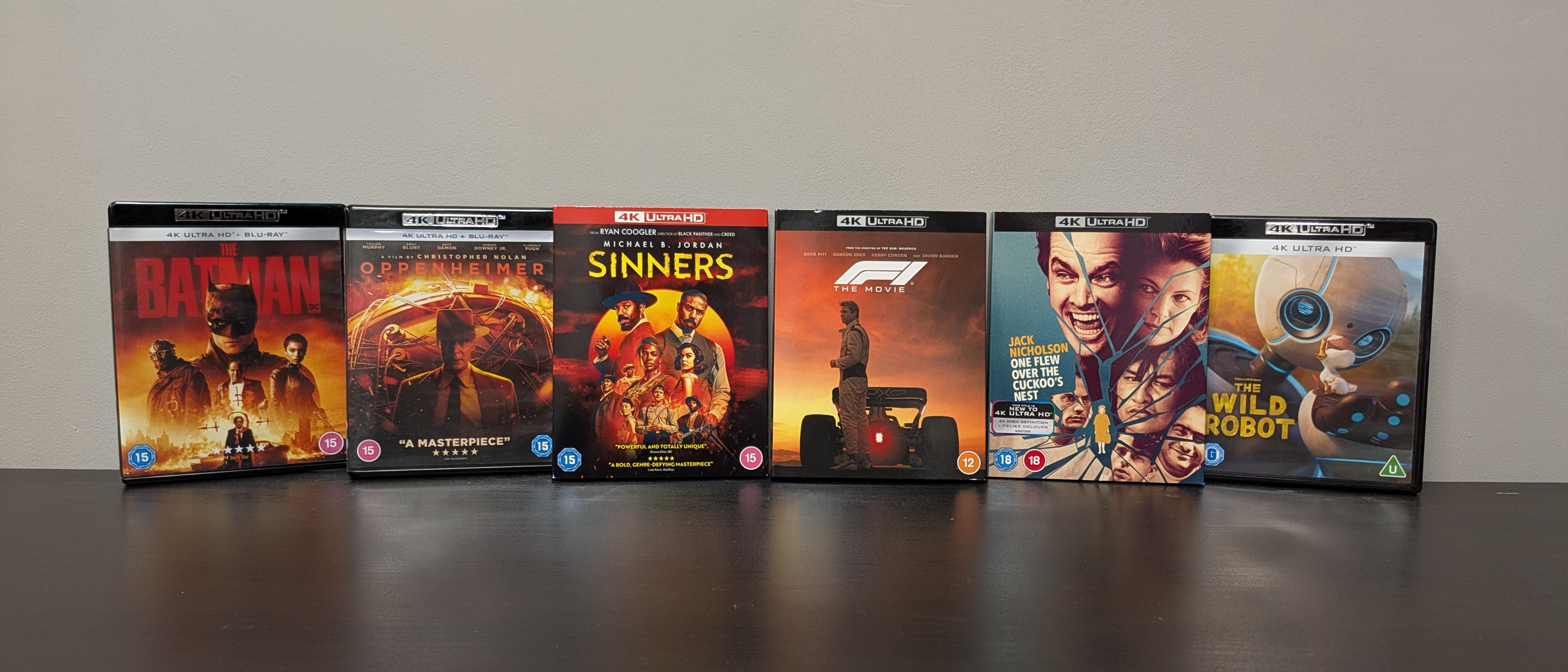 The Batman, Oppenheimer, One flew over the cuckoo's nest, F1, Sinners and The Wild Robot 4K Blu-ray cases lined up against wall 