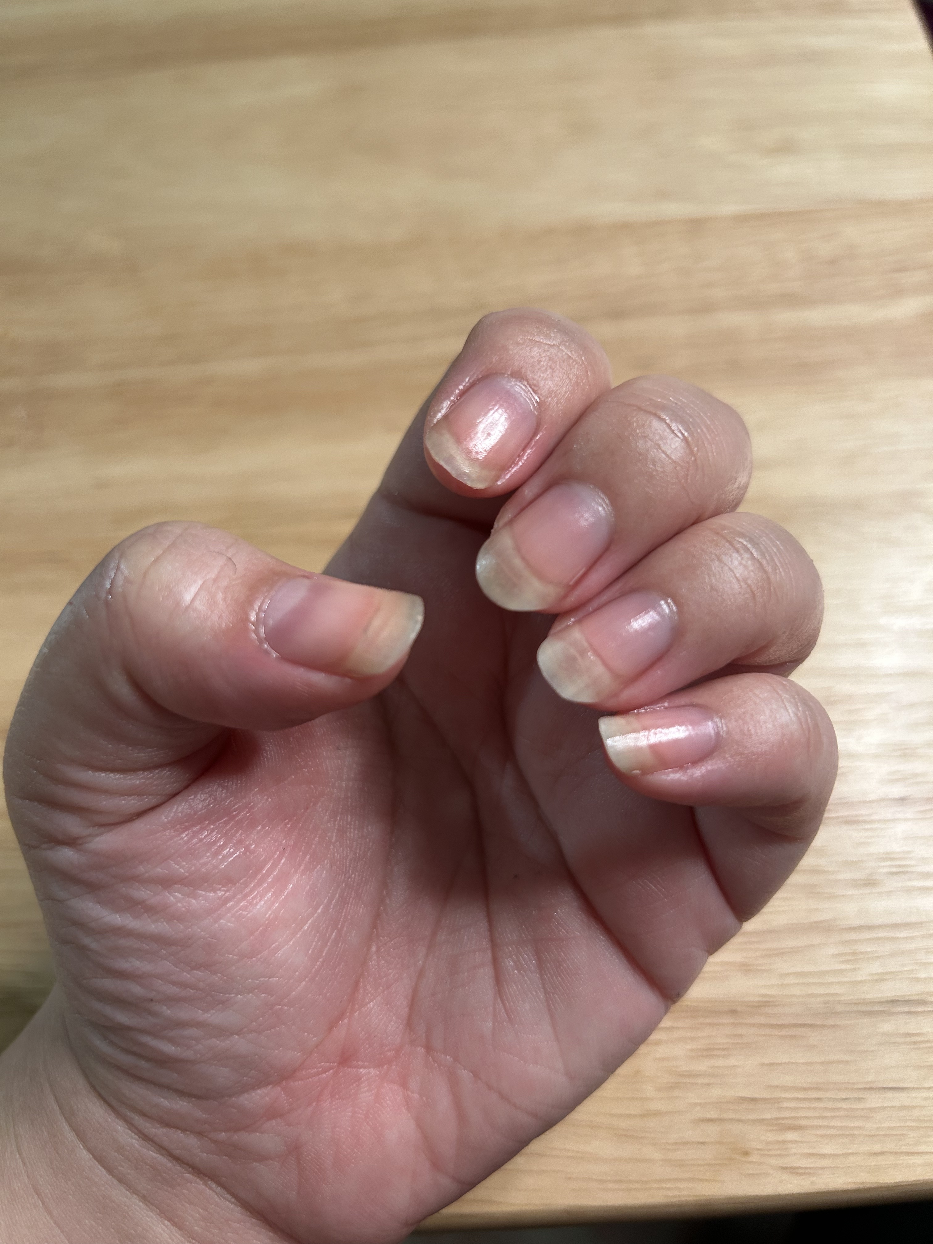 A woman's hand and nails before after cuticle oil with a wood background and shiny nails.