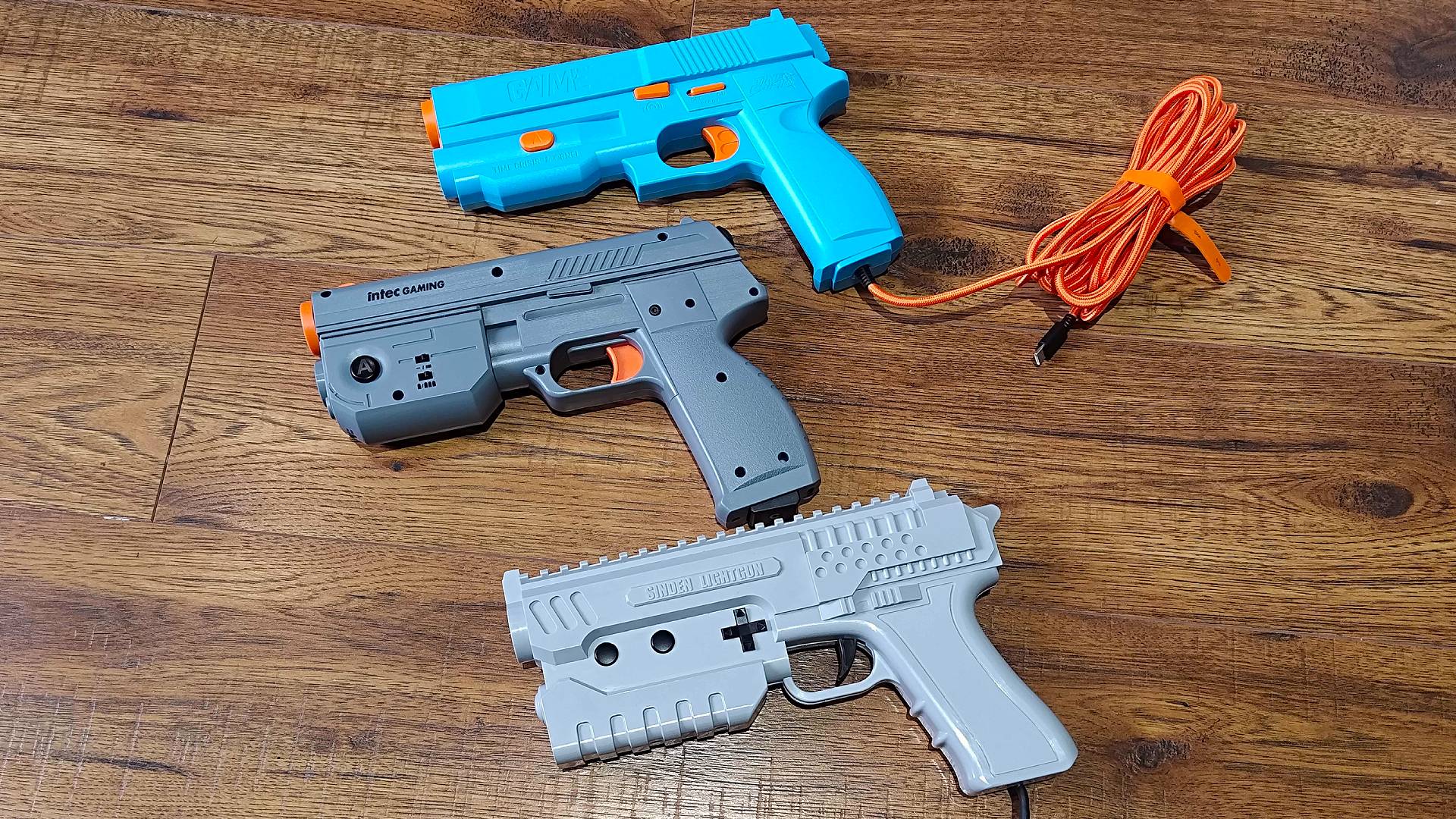 Intec Time Breaker Lightgun with G'AIM'E Lightgun above and Sinden Lightgun below on woodgrain floor.