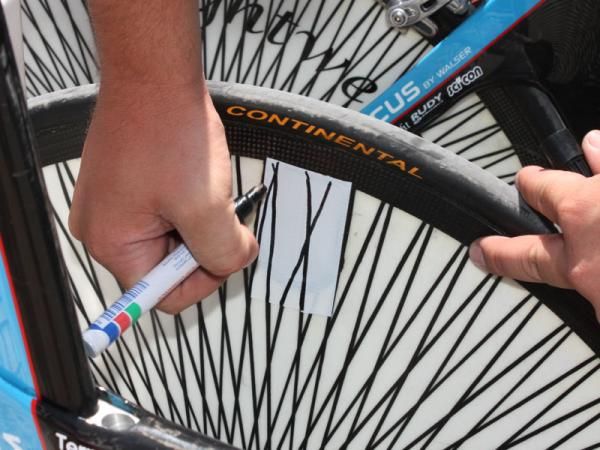 A team mechanic seals up the valve access hole with white tape then draws in the spokes with a marker. Not a shabby job, either, considering he was doing the work freehand and with an upside-down view.