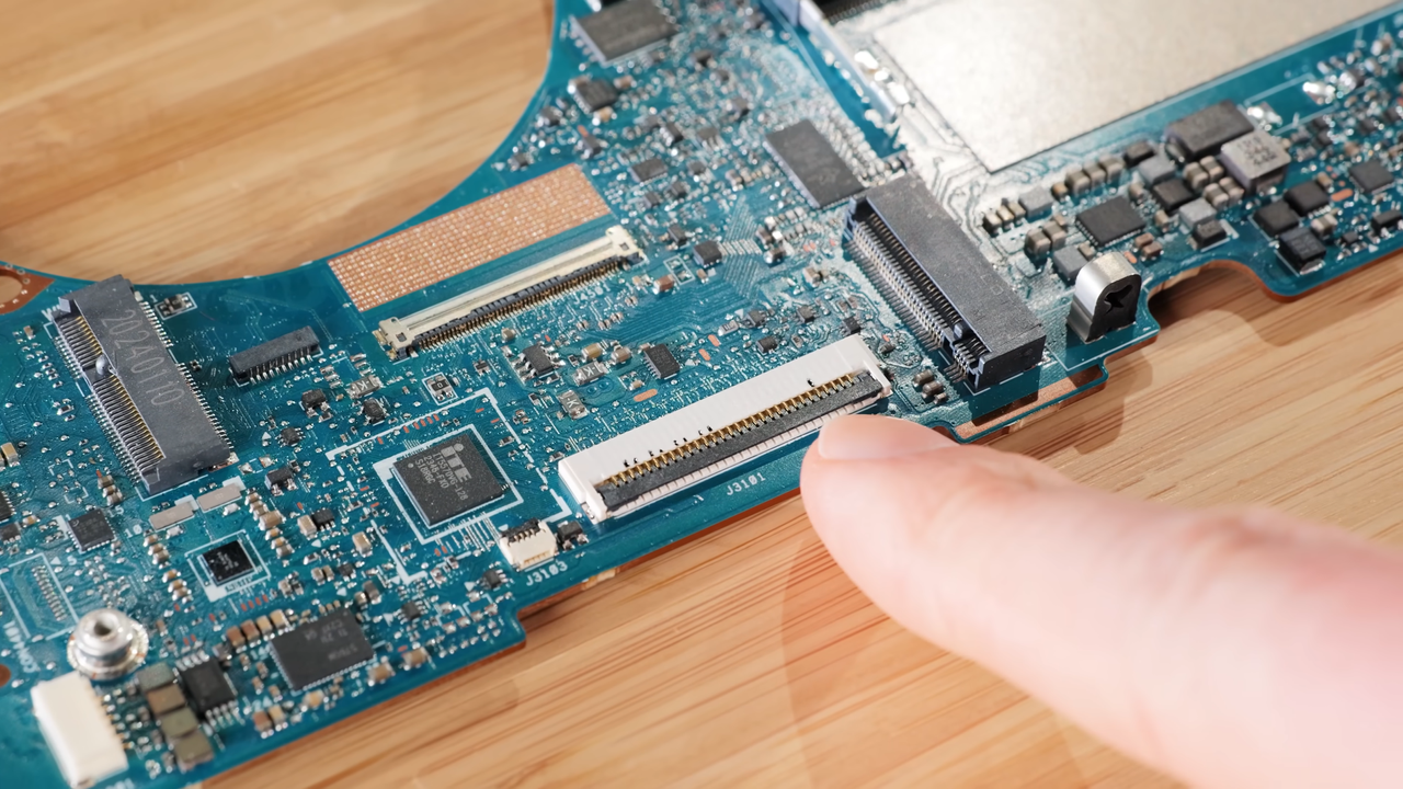 Close up of RTX 4060 laptop motherboard keyboard ribbon cable connector with finger pointing at pins.