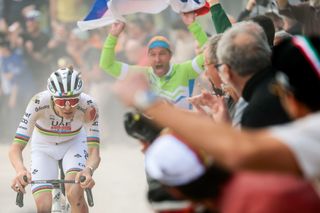 Tadej Pogacar riding solo as a Slovenian fan holds up a flag behind him