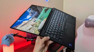 The Lenovo ThinkPad X1 Carbon (Gen 13) Aura Edition held in the air with its display opened all the way.