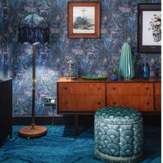 living room with patterned blue carpet, wooden side cabinet, blue patterned wallpaper, blue patterned pouffe, blue patterned floor lamp