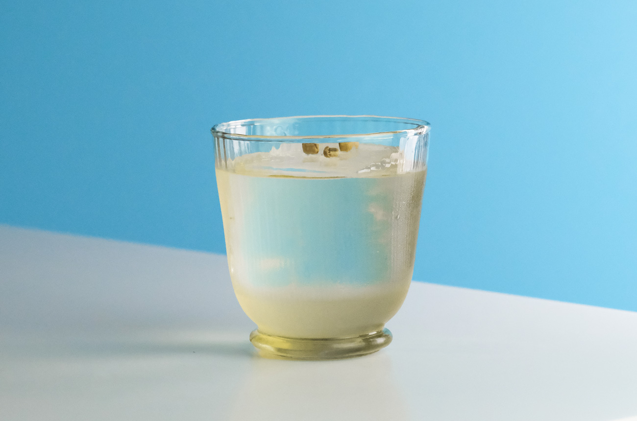 Cocktail glass with large ice cube against a white and blue background