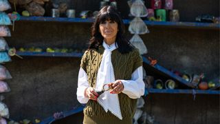 Claudia Winkleman is pictured wearing a green sweater vest, white shirt and with bright orange nails in season three of the BBC's The Traitors