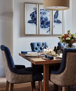 Dining table with upholstered blue dining chairs, table laid for a meal and a framed photograph of a turtle on the wall.