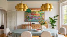 a white dining room with large arched doors and windows are either end, A blue painted accent ceiling and two brass statement pendants that hang over the table