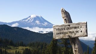 A sign for the Pacific Crest Trail with a snow capped Mount Adams in the background