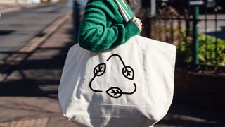 Midsection of young woman carrying reusable shopping with a recycling symbol.