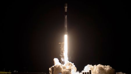 a white and black rocket lifts into the predawn sky, lighting its launch pad and ground below