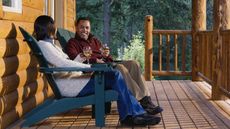 A couple smile at each other as they sit on the porch of their dream home and drink wine.