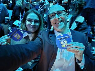 Lance and Viktoria taking a selfie at Samsung's Galaxy Unpacked, in dramatic blue lighting, each holding up their Galaxy badge