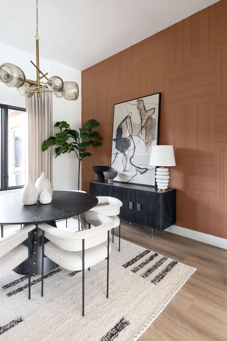 Dining room with patterned terracotta wallpaper on accent wall, white remaining walls, black dining table and sideboard and white dining chairs