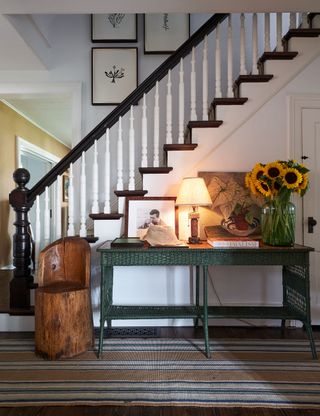 hall and stairs with striped runner and white banisters and green rattan side table and rustic wooden seat
