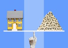 Miniature model of yellow single family home and a pile of money bags balancing on monochromatic woman's finger, striped blue background.