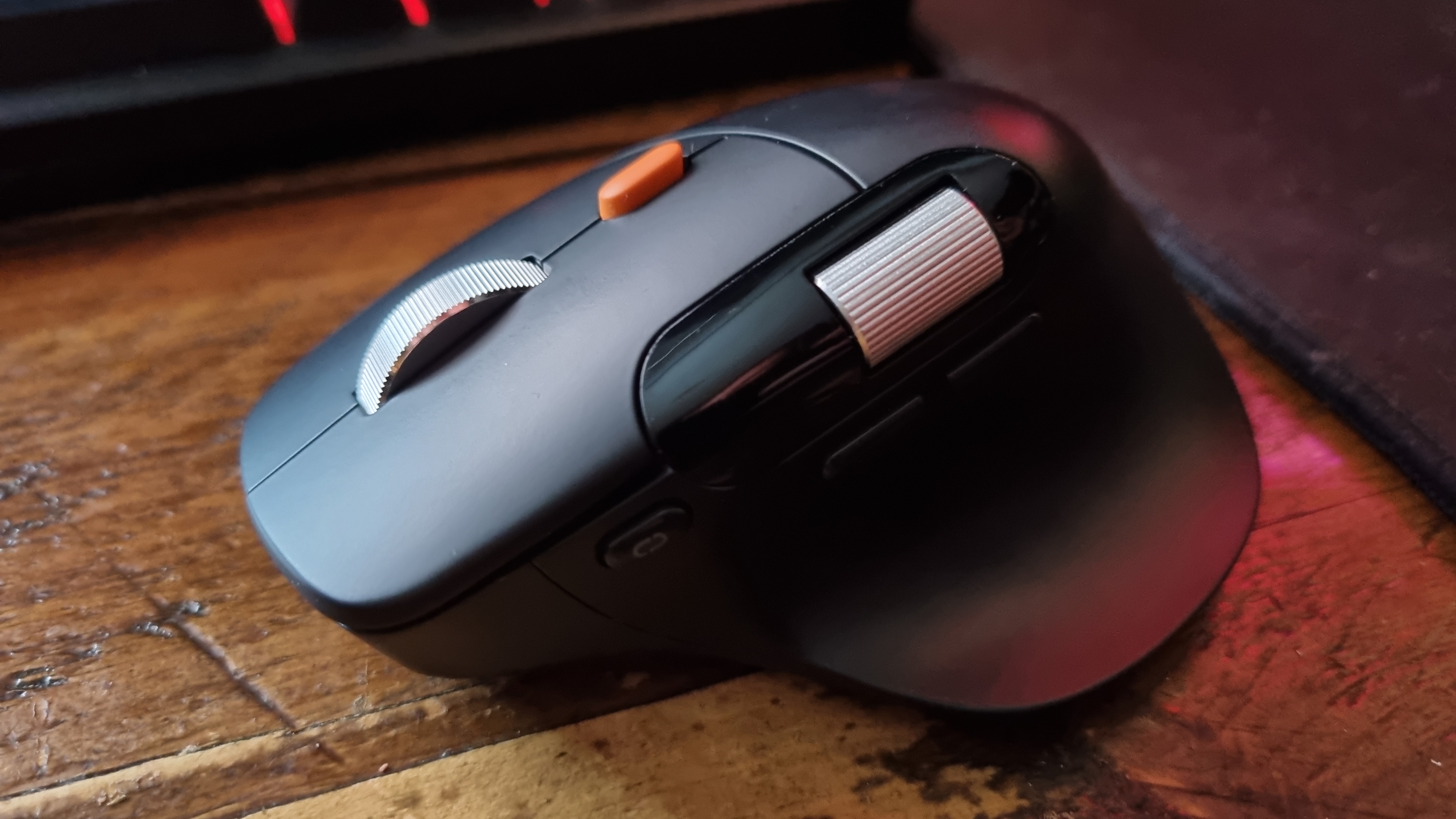 A ProtoArc EM25 ergonomic mouse on a wooden desk, in front of a mouse pad