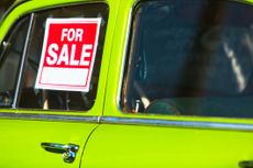 A "for sale" sign is in the window of an old, bright green car.