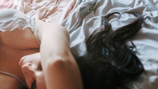 brunette girl with hair lying on the bed with her arms over her head - stock photo