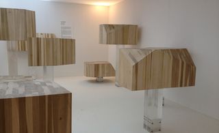 Interior room, white walls, ceiling and floor, wooden block sculptures on clear stands. light in the top corner of the room