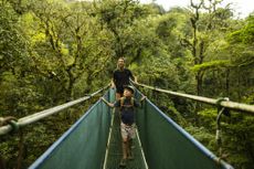 A father and son walk on a suspension bridge in Costa Rica on holiday travel.