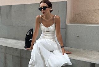 Debora Rosa wearing a white sundress with black sunglasses and a black purse.