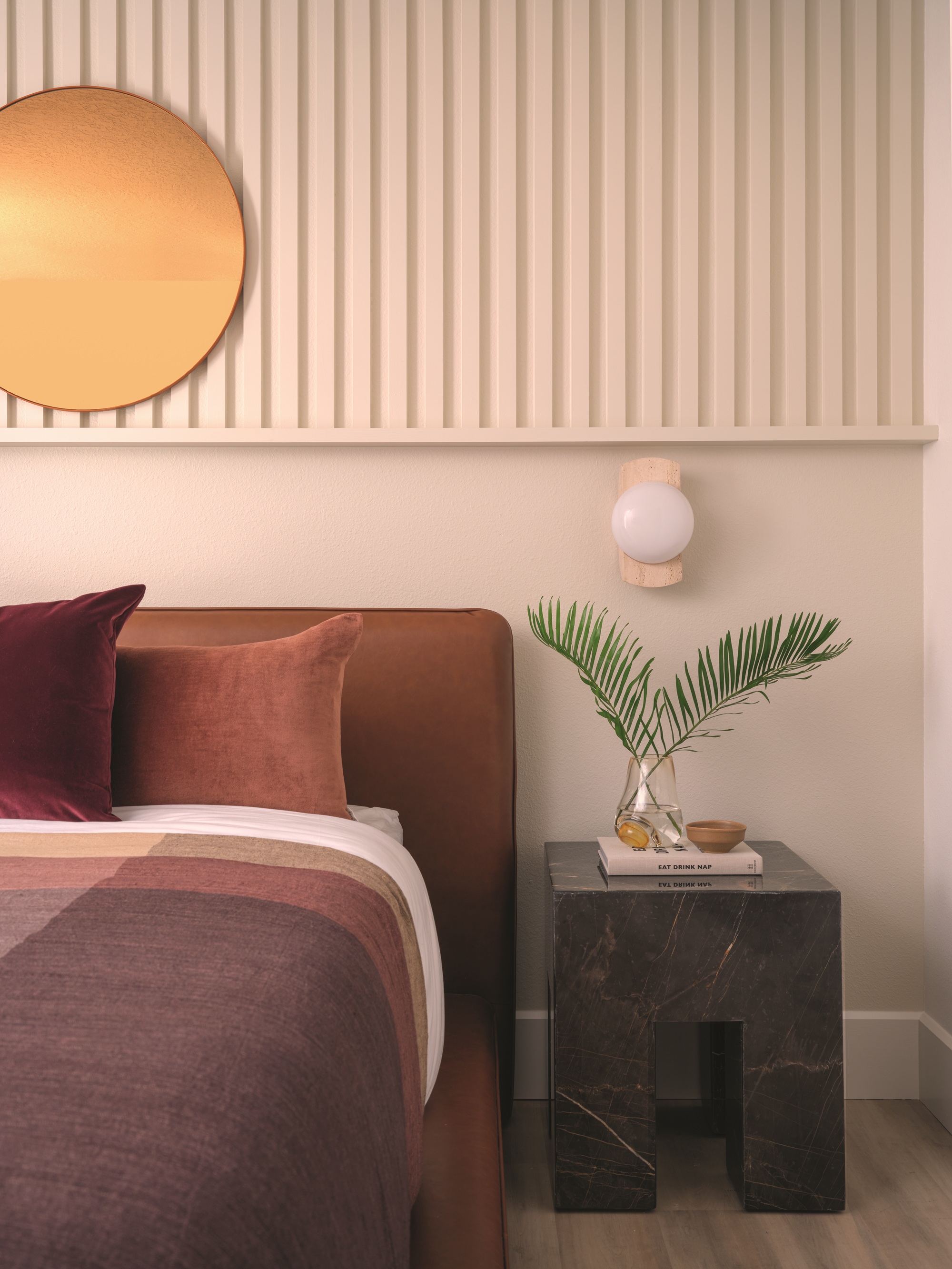 a beige bedroom with a rust colored bed with neutral styling and a marble nightstand
