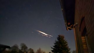 streaks of fire blaze the the night sky above a house.