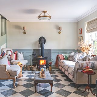 Living area with sofa and armchairs surrounding ottoman and wood burner on chequered floor