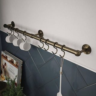 A brass kitchen rail with antique brass hooks to hold mugs and utensils 