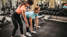 A personal trainer coaches a woman to deadlift using dumbbells correctly