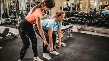 A personal trainer coaches a woman to deadlift using dumbbells correctly